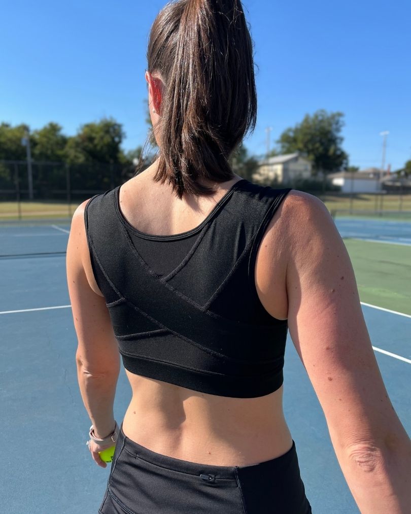 Woman wearing the Pipperly Empower posture support sports bra on a tennis court showing the supportive back panel design